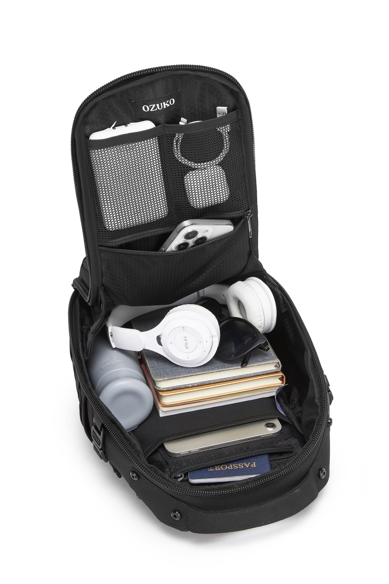 Daytrip Backpack 12L in Black - top-down view of the packed main compartment with headphones, sunglasses, notebooks, a water bottle, a phone, and a passport
