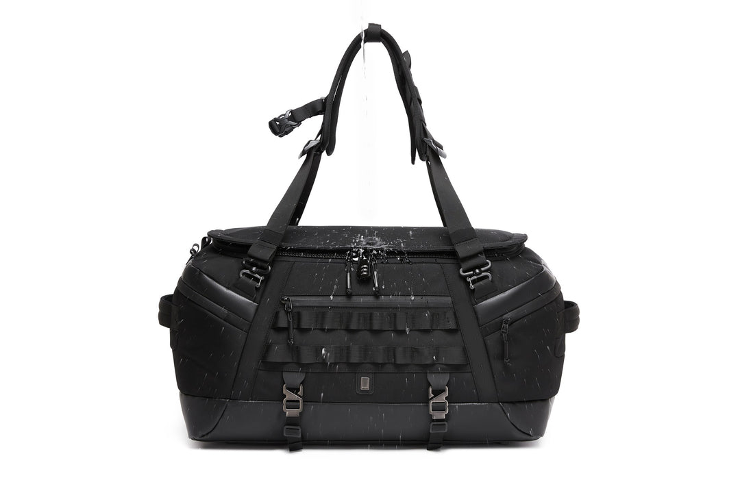 Black Cargo Duffel 45L, front view, with water poured over the top to demonstrate the water-resistant coated exterior; combination lock and MOLLE webbing visible on the front panel